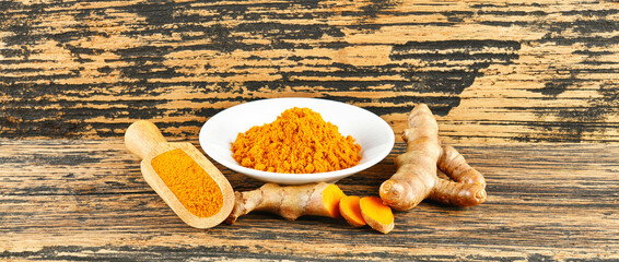 Turmeric powder and fresh turmeric on wooden background.