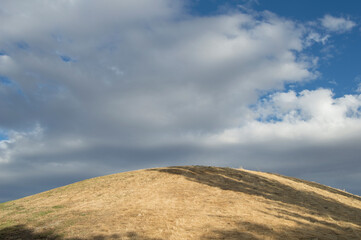 a hill in a park with dry grass and sky background with clouds in summer
