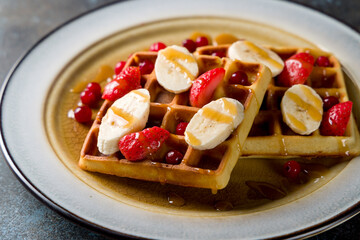 waffles with fresh strawberries, bananas and powdered sugar on blue stone table