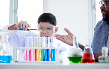 A Caucasian male student raises a glass vial of various colored liquids while a teacher guides him in a science chemistry laboratory