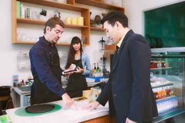 A young Caucasian barista couple was chatting with Asian customers. At the counter in cafes and restaurants, entrepreneurial concept Starting a small business, lifestyle, food, and beverage, cafe