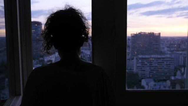 A woman looks at the city from her window at sunset, in Paris, France