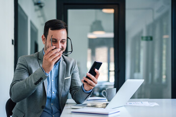 Happy manager wearing eyeglasses while text messaging on cellphone at office