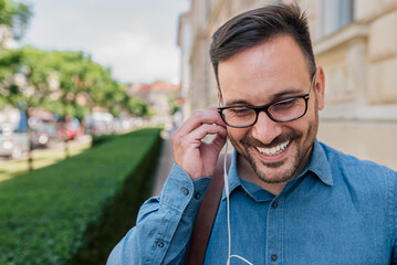 Smiling businessman listening music through headphones on sidewalk at the city