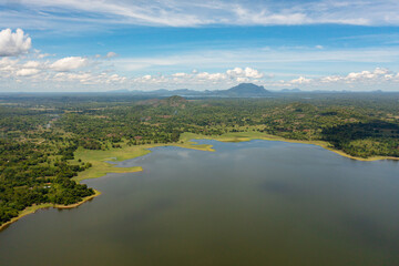 Aerial view of Sorabora lake in sri lanka with wooded hills. Lakeside scenery under a blue cloudy...