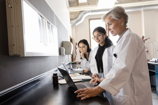 Female college professor and students using laptop in science laborato