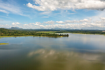 Aerial drone of valley with a lake and tropical vegetation against a blue sky and clouds. Sorabora lake, Sri Lanka.