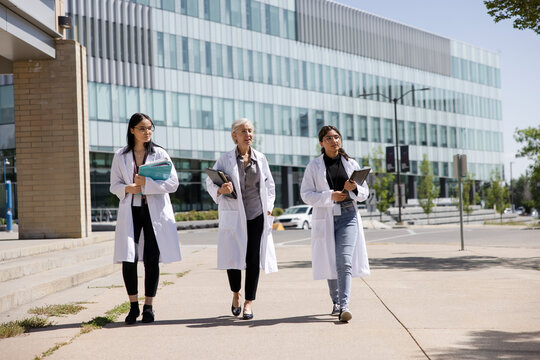 Female college professor and students walking on sunny campus
