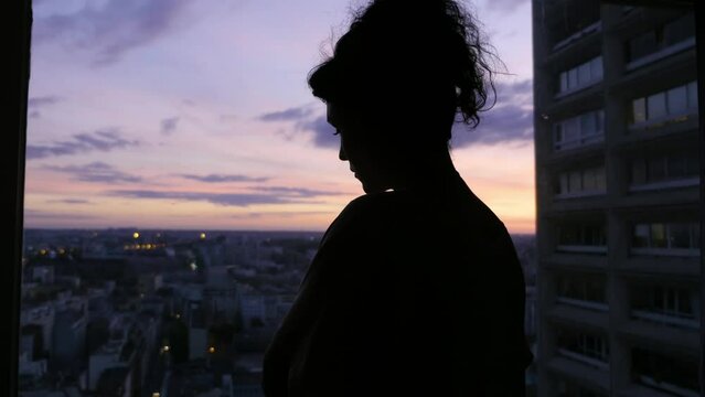 A woman watches the sunset from the window of her building 2
