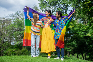 group of lgbtq community movement in rainbow colorful clothes are having fun while raising rainbow flags together in the park. lgbtq pride month concept