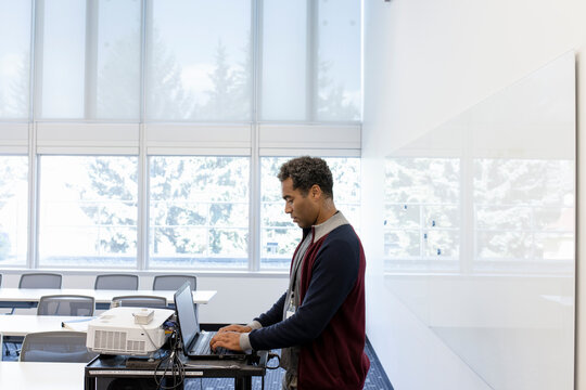 Male College Professor Using Laptop In Classroom