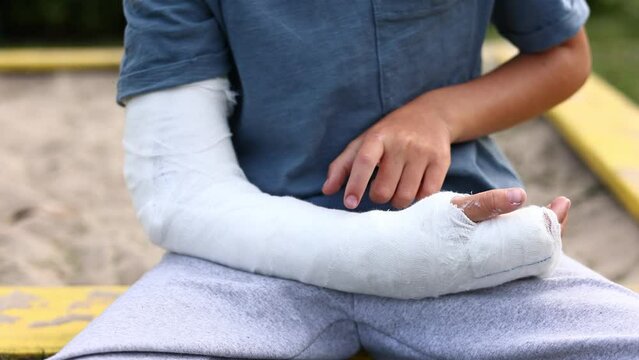 little boy with a fractured limb outdoors. a child's arm is broken. fracture injury in the summer holiday. kid is touching plaster cast on the arm