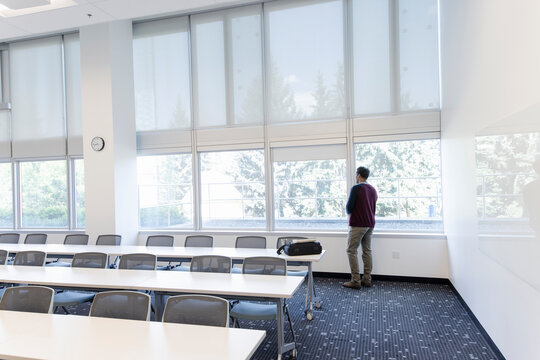 Male college professor looking out window in empty classroom