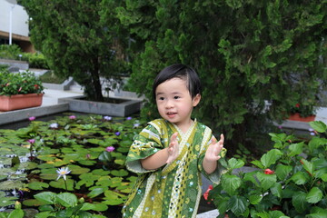 a child clapping hands at a water lily garden, dressed up in Japanese costume 