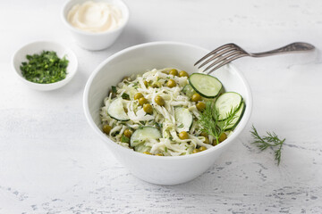 Salad with white cabbage, green peas, cucumber, herbs and mayonnaise sauce on a light blue background