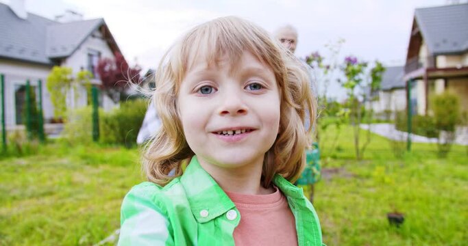 POV from small cute boy son taking video in garden and waving hands father with grandfather planting trees in garden. Videochat. Summer work at village house. Videochatting. Outside.