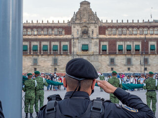 A Mexican Police officer maintains salute as soldiers wrap flags during the Zocalo Square Flag...