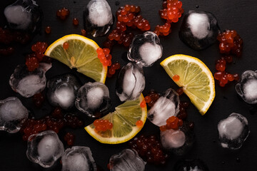 Lemon slices with red salmon caviar and ice cubes on a black wooden table background. Background...