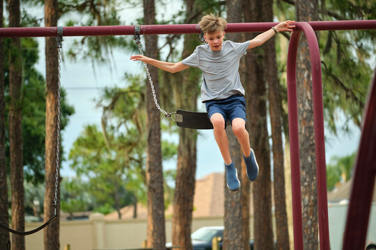Young handsome smiling teenage boy jumping out of the swings on summer vacations sunny day. Danger of accident concept