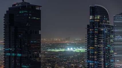 Aerial view of housing development promenade with JLT district skyscrapers and artificial lake with a park night timelapse.