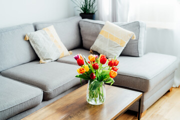 Vase of fresh tulips on the coffee table with blurred background of modern cozy light living room...