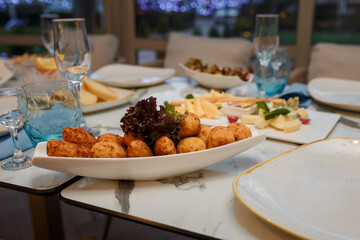 Festive table with appetizers. Cheese and meat plates with greenery. Empty glasses, plates for guests