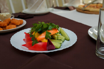 Festive table with appetizers. Vegetable plate of cucumbers, bell peppers, tomatoes, dill and parsley greenery. Nuggets and pizza on background