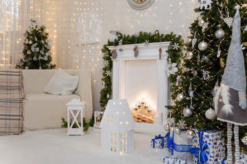 Christmas decorations. White sofa and fireplace, christmas tree decorated with white bulbs, toys and shiny garlands. Happy New Year