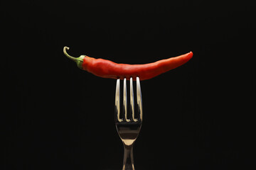 Red pepper on a fork on a black background. Close-up