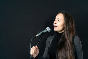 Young Asian or Caucasian brunette woman in casual clothes holding mic and singing song alone in...