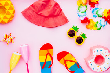 Flat lay of summer vibes concept with colorful pool party items, funny sunglasses, cocktail glasses. inflatable drink holders, flip flops, bucket hat, flower necklaces on pink background. Copy space