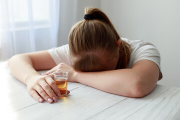female alcoholic sleeps on a table with a stack of strong alcohol