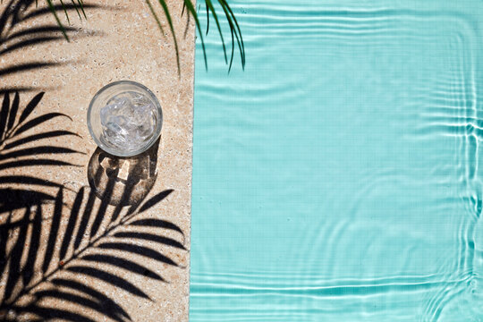 Top view swimming pool with glass of water and palm shadows. Summer vacation concept.
