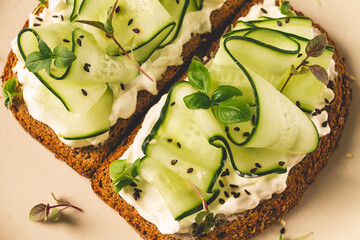 Breakfast, cereal bread sandwiches, cream cheese, sliced cucumber, with micro greenery on a light table, close-up, top view, selective focus, no people,