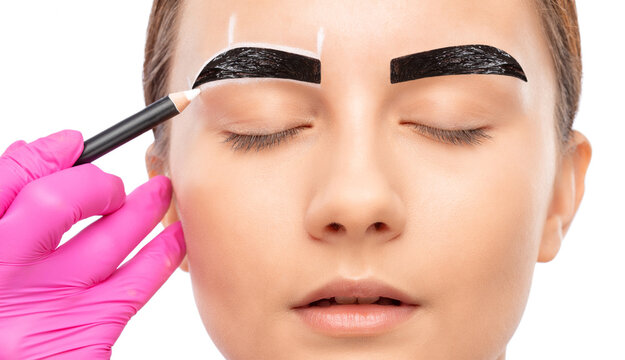 The make-up artist makes markings with a white eyebrow pencil and applies paint on the eyebrows. Professional make-up and face care.