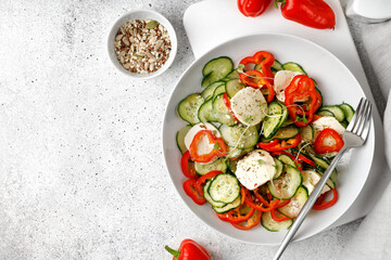 Green fresh salad with cucumbers, sweet peppers, feta cheese on white  plate, on grey background, top view.