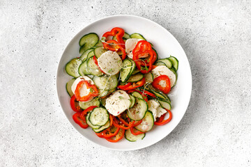 Green fresh healthy Sliced salad with cucumbers, sweet peppers, feta cheese,  on white plate on grey background, top view. Copy space, place for text.