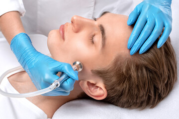 Obraz na płótnie Canvas A cosmetologist is making the procedure Microdermabrasion of the facial skin in a beauty salon. Cosmetology for men and professional skin care.