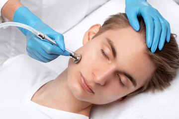 A cosmetologist is making the procedure Microdermabrasion of the facial skin in a beauty salon. Cosmetology for men and professional skin care.