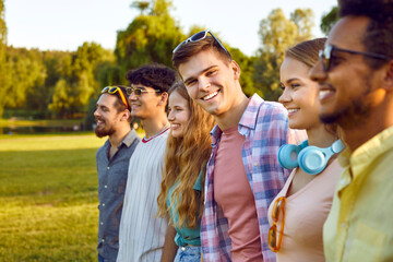 Portrait of joyful young man standing with his friends hanging out in public park. Cropped shot of group of cheerful multiracial friends gathered together in park on sunny summer day. Selective focus.