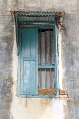 An open window with grilles and a sheet metal roof in the facade of an old house, Penang, Malaysia.
