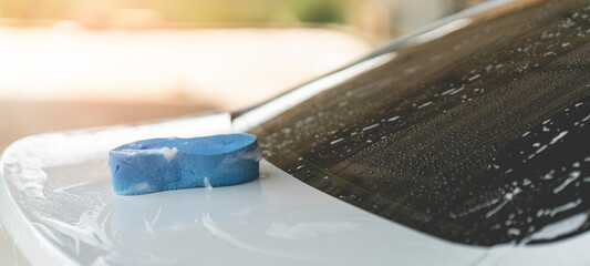 A car wash sponge filled with car washing foam is placed on the trunk lid. - obrazy, fototapety, plakaty