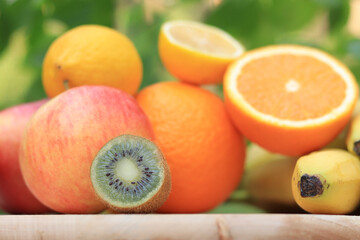 A group of ripe fruits photographed with selective focus. Fruit harvest on nature background. Oranges, kiwi, lemons, apple, bananas, some are cut