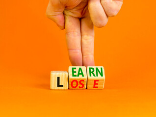 Learn or lose symbol. Concept words Learn and Lose on wooden cubes. Businessman hand. Beautiful orange table orange background. Business and Learn or Lose concept. Copy space.