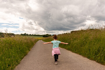 Fototapeta premium A small child runs in the middle of a field along the road with his arms apart