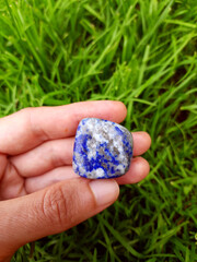 Lazurite mineral stone in the hand on green grass background, natural gemstone for healing, meditation, altar, spiritual practice, reiki, ritual.