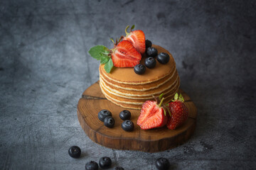 Pancakes with strawberries, blueberries and honey on a wooden plate.