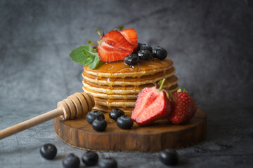 Pancakes with strawberries, blueberries and honey on a wooden plate.