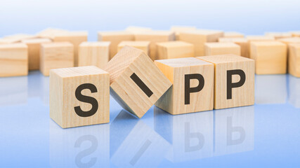 four wooden blocks with the letters SIPP on the bright surface of a blue background. the inscription on the cubes is reflected from the surface. business concept.