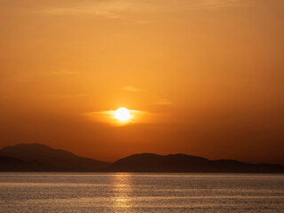 Sea beach and colorful sunset sky. Panoramic beach landscape. Seascape and a distant island in the background. Orange and golden sunset sky, calmness, tranquil relaxing sunlight, summer mood.